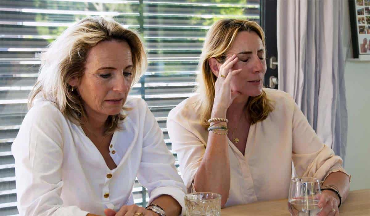 Zussen Saskia en Winnie zitten met gesloten ogen aan tafel in het huis in Apeldoorn tijdens het programma De Moeite Waard?!