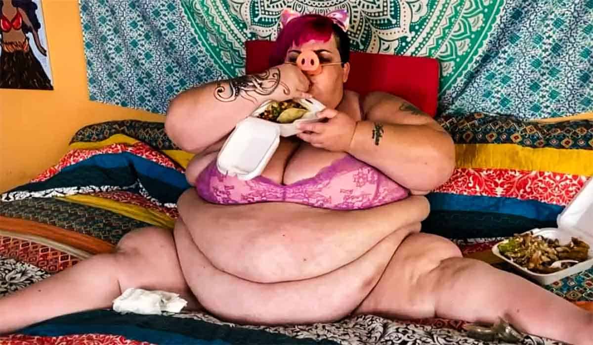 Half ontblote vrouw met rood haar en imitatie varkensneus zit op bed te eten in de RTL 5 docu Feeders.