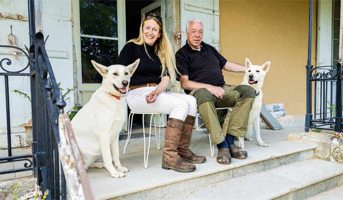 Voormalig Ik Vertrek deelnemers Emmy Postma en Rutger poseren zittend met hun twee witte honden voor B&B Chateau Chauvaux in Frankrijk. Beeld bron: Kasteelvrouwe Emmy en Rutger | © Elvin Boer/MAX